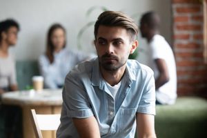 frustrated shy man sitting away from people.