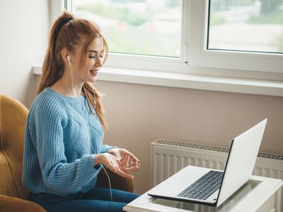 Side view photo of a caucasian woman with red hair and freckles explaining something at laptop wearing earphones