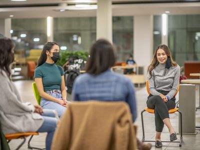 Multi-ethnic group of young adults in group support set up and sitting on chairs.