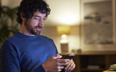 Handsome businessman using smart phone at home. Male professional is looking at mobile phone. He is working late