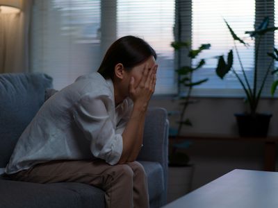 Depressed woman sitting on sofa with her hands on her face