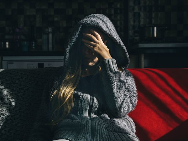 A young woman in a hoodie is sitting on a red sofa at home. The concept of depression and mental disorders.