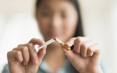 Woman breaking cigarette in half, quitting smoking.