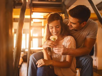 Affectionate man surprising his girlfriend with a carnation flower while sitting on staircase at home.