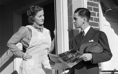 Salesman At Door Of A House Wife Showing Her A Brochure Of His Product