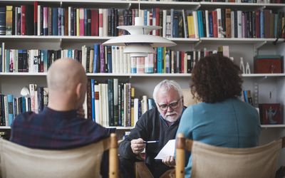 Senior therapist explaining analysis to mature couple against bookshelf at home